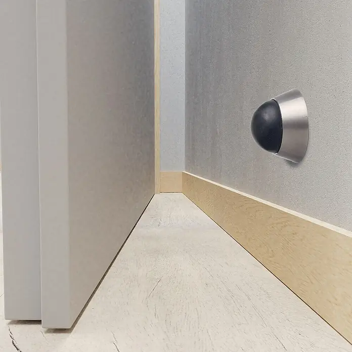 Wandtürstopper - Ø x H: 40 x 25 mm - Nahaufnahme eines Türstoppers an einer grauen Wand neben einer Tür, der den Türgriff vor Beschädigungen schützt.