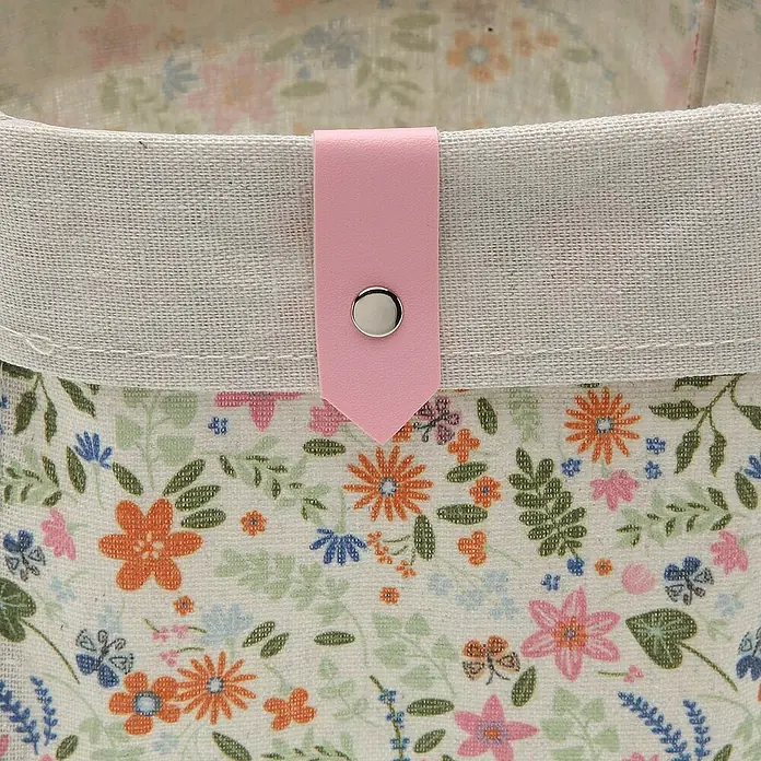 Versa Juego de cestas - Flores rosado, 3 ud. - Primer plano de una cesta de tela con estampado floral con lengüeta rosa y botón plateado.