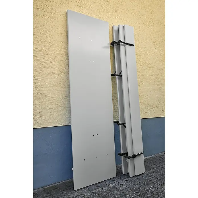 Bierzeltgarnitur - 3 -tlg., Fichte/Stahl, Klappbar, Beige/Grau, Tisch (L x B x H): 220 x 70 x 77 cm, Bank (L x B): 220 x 30 cm - Eine graue Klapptischplatte lehnt an einer Wand, daneben ein zusammengeklappter Tisch. Praktisch für flexible Raumnutzung.
