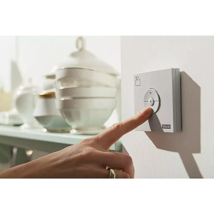 Velux Solar-Nachrüst-Set KSX 100K - Passend für: VELUX Schwingfenster GGU/GGL CK04 – UK10 - Eine Hand drückt einen VELUX-Wandschalter. Der VELUX-Schalter steuert Fenster und Rollläden und bietet Komfort und Energieeffizienz.