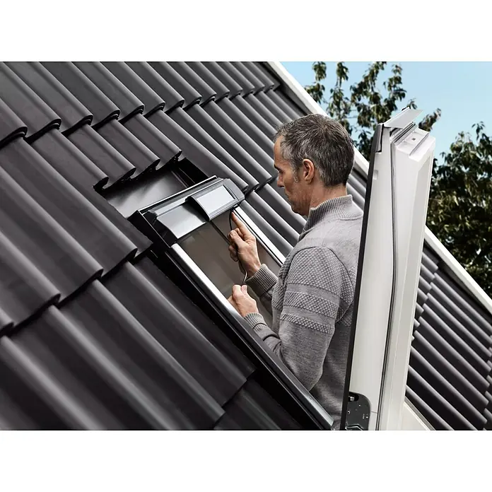 Velux Solar-Nachrüst-Set KSX 100K - Passend für: VELUX Schwingfenster GGU/GGL CK04 – UK10 - Ein Mann montiert ein Dachfenster auf einem Ziegeldach, wobei der Fokus auf der Installation und dem Fensterdesign liegt.
