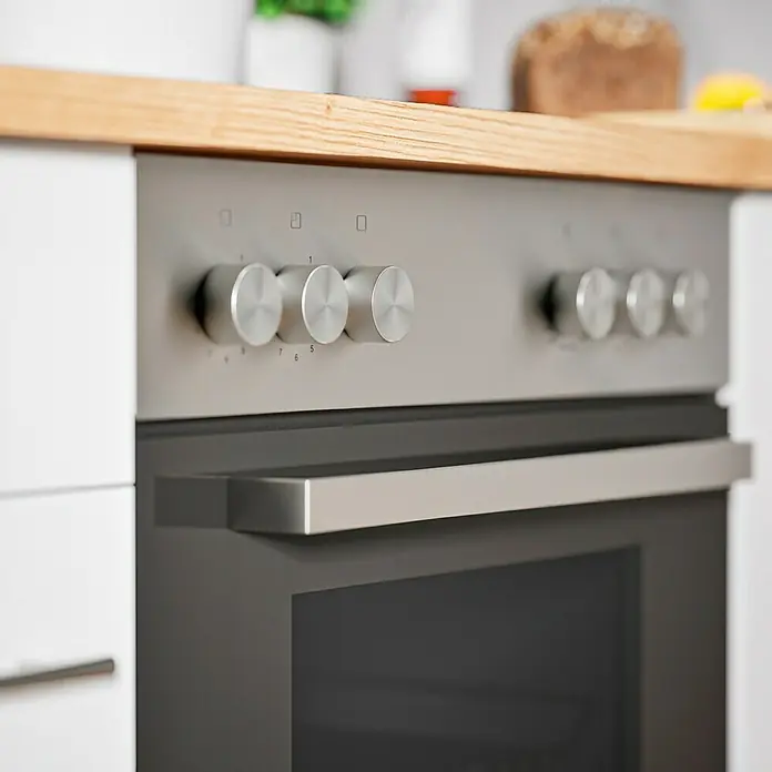 Respekta Composición de cocina Hilde - Ancho: 310 cm, Blanco, Con electrodomésticos - Primer plano de un horno moderno plateado con mandos de control y un asa, integrado en un mueble de cocina blanco con una encimera de madera.