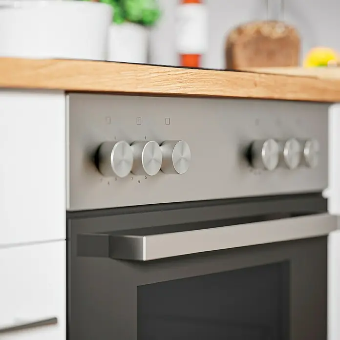 Respekta Composición de cocina Hilde - Ancho: 250 cm, Blanco, Con electrodomésticos - Primer plano de un horno moderno de acero inoxidable con pomos y asa, integrado en un mueble de cocina luminoso con encimera de madera.