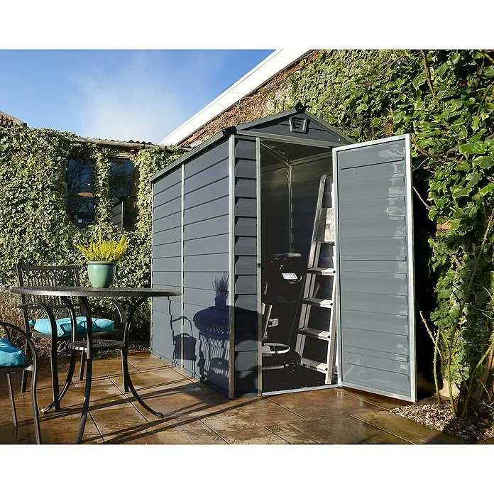 Palram – Canopia Gartenhaus Skylight - Außenmaß inkl. Dachüberstand (B x T): 121 x 177 cm, Kunststoff, Anthrazit/Grau - Eine graue Gartenhütte mit geöffneter Tür, die einen Blick auf eine Leiter und Gartengeräte im Inneren freigibt.
