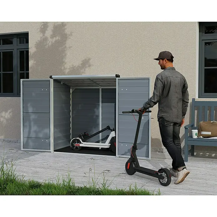 Palram – Canopia Arcón Voyager - L x An x Al: 90 x 139 x 146 cm, Gris oscuro, Policarbonato - Una caja de equipos gris con dos patinetes eléctricos delante y dentro. El lugar ideal para guardar tus herramientas de jardín y e-scooters.