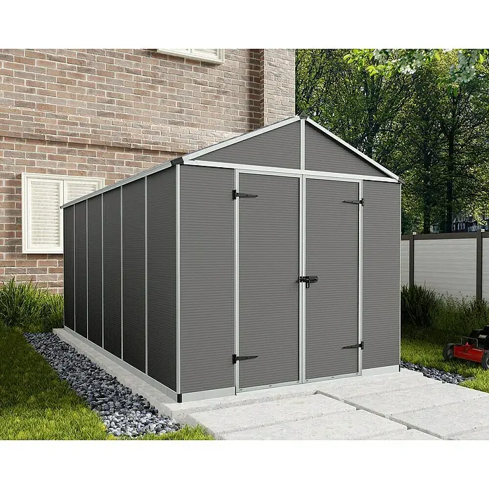 Palram – Canopia Gartenhaus Rubicon - Außenmaß inkl. Dachüberstand (B x T): 2,37 x 4,52 m, Kunststoff, Grau - Ein geräumiges, graues Gartenhaus mit Doppeltür und silbernen Rahmen steht neben einem Backsteingebäude.