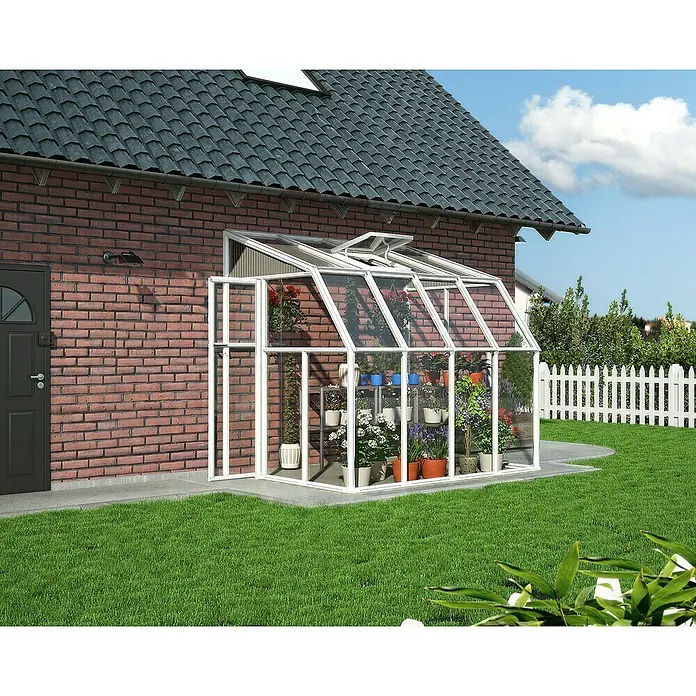 Palram – Canopia Terraza Solarium Sun Room - Medidas ext. (An x Pr): 260 x 200 cm, Plástico, Blanco - Primer plano de un invernadero con plantas y flores, sobre un edificio de ladrillo y un césped.
