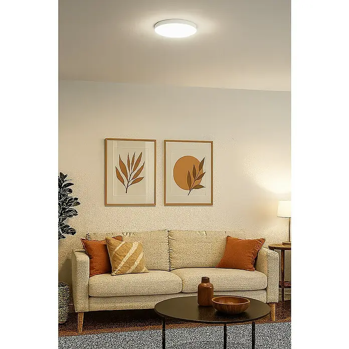 Alverlamp Plafón LED redondo - 20 W, Ø x Al: 22,5 x 3,9 cm, Blanco, Blanco frío - Una lámpara de techo moderna en un salón con sofá y cuadros enmarcados. Su diseño minimalista proporciona una iluminación uniforme.