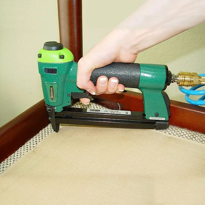 Prebena Druckluftnagler 1XR-A16 - Betriebsdruck: 4 bar - 7 bar, Passend für: Prebena Heftklammern der Type A von 4 - 16 mm - Nahaufnahme einer Hand, die einen grünen Prebena-Drucklufttacker zum Befestigen von Stoff an einem Holzrahmen verwendet.