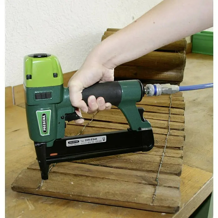 Prebena Druckluftnagler 2XR-ES40 - Betriebsdruck: 4 bar - 7 bar, Passend für: Heftklammern der Type ES von 15 - 40 mm - Eine Prebena 2XR-ES40 Klammergerät in Grün mit einem schwarzen Griff und einem blauen Luftschlauch befestigt Holzlatten auf einer Werkbank.