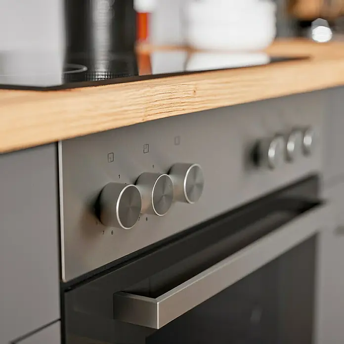 Respekta Cocina esquinera Hilde - Ancho: 310 cm, Gris, Efecto madera, Con electrodomésticos - Primer plano de un horno gris moderno con mandos plateados y bandeja de madera.
