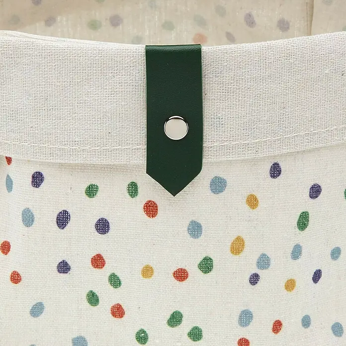 Versa Juego de cestas - Dotty, Poliéster - Primer plano de una cesta de almacenamiento de tela con lunares de colores y cierre verde oscuro con botón plateado.