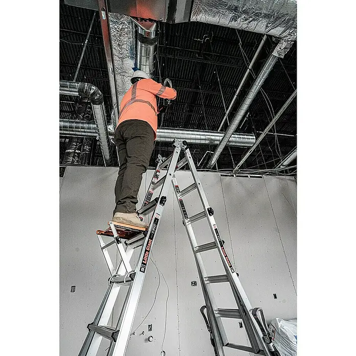 Little Giant Trittablage Platform Pro® - Belastbarkeit: 150 kg - Ein Bauarbeiter steht auf einer Little Giant Leiter und arbeitet an einem Lüftungskanal an der Decke in einem unfertigen Gebäude.