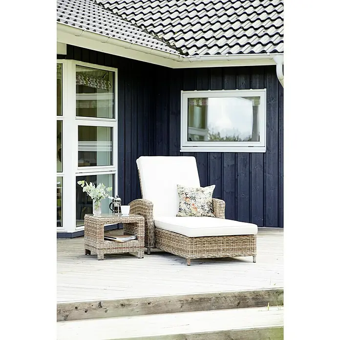Tumbona de jardín Gotland - 83,5 x 206 x 26 cm, Arena, Acero, Respaldo regulable - Una tumbona de ratán con una mesa auxiliar en una terraza de madera, creando una relajante escena al aire libre.