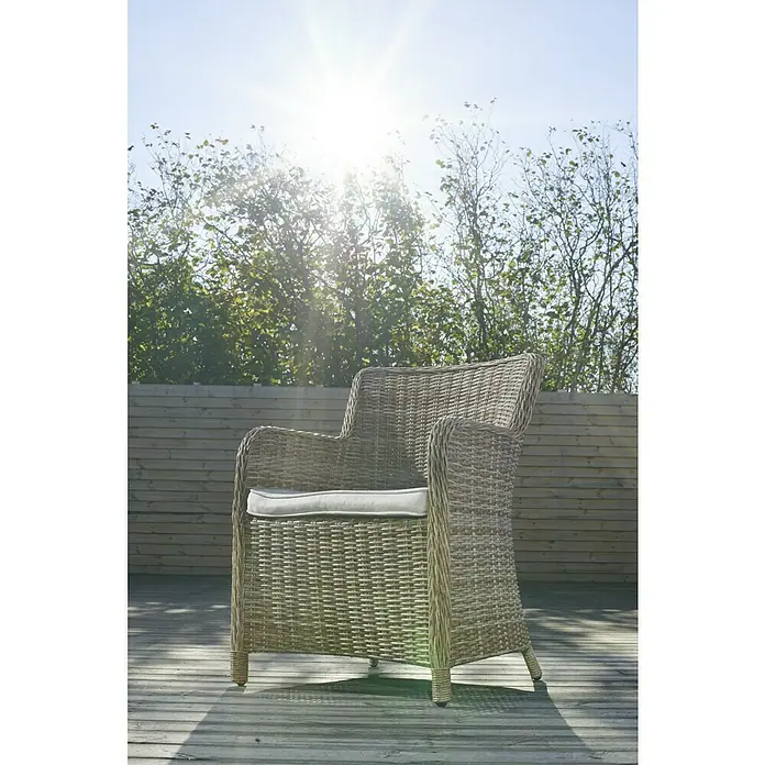 Sillón de jardín Gotland - An x Pr x Al: 79 x 63 x 99 cm, Arena - Primer plano de una silla de ratán con cojín color crema en una terraza de madera en un día soleado, rodeada de árboles.