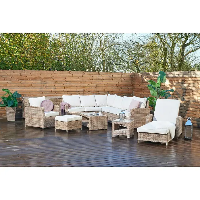 Taburete reposapiés Gotland - L x An x Al: 61 x 51 x 40 cm, Arena - Acogedor juego de asientos de ratán para exteriores con suaves cojines blancos colocados sobre una terraza de madera frente a una valla de madera.