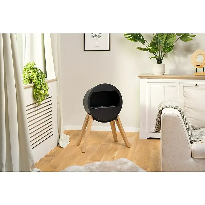 Aduro Bioethanol-Kamin B2 - 46 x 63 x 70 cm, Schwarz - Ein runder, schwarzer Mediaschrank mit Holzbeinen steht auf einem Holzboden in einem hellen Wohnzimmer.