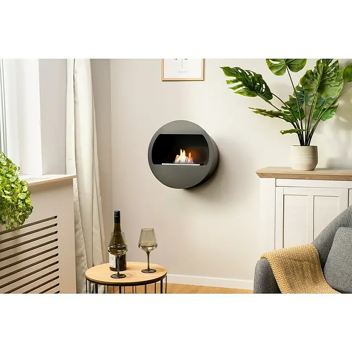 Aduro Bioethanol-Kamin B2 - 46 x 63 x 70 cm, Schwarz - Ein modernes Interieur mit einem runden Wandkamin, der für eine gemütliche Atmosphäre sorgt, begleitet von einer Flasche Wein und Gläsern.
