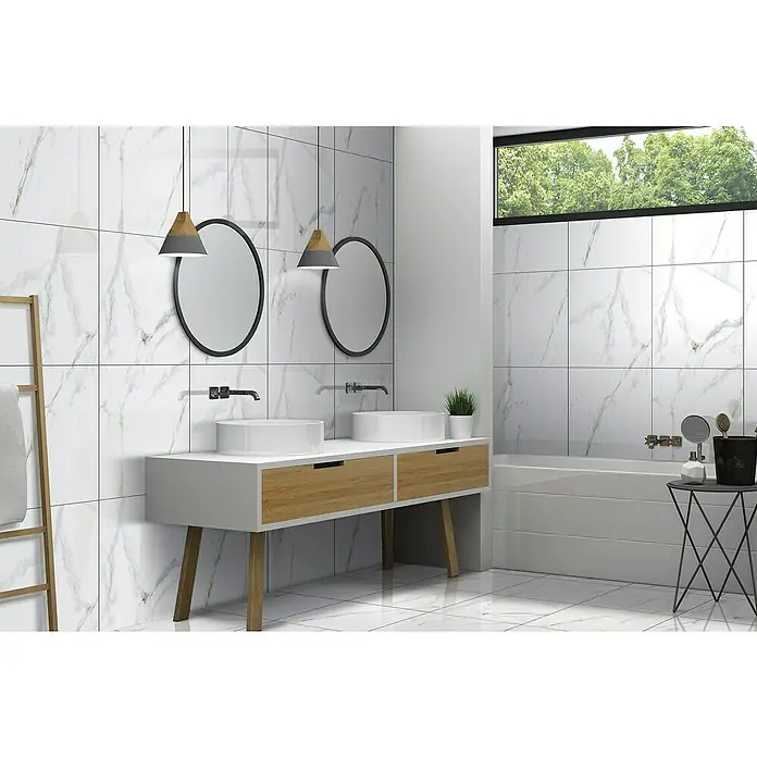 Feinsteinzeugfliese Calacatta - 60 x 60 cm, Weiß/Gold, Glänzend - Badezimmer mit weißen Marmorfliesen, zwei Waschbecken mit Holzunterschränken und runden Spiegeln. Elegante und moderne Gestaltung.