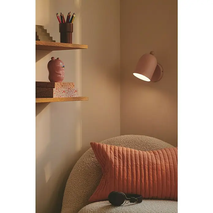 Nordlux Aplique de pared Gaston - 15 W, An x Pr x Al: 11,5 x 19,5 x 19,5 cm, Rosa, E27 - Lámpara de pared rosa suave junto a una silla cómoda con auriculares, ideal para un rincón de lectura.