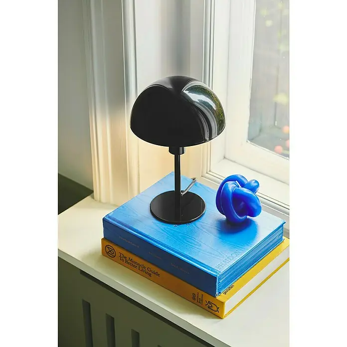 Nordlux Lámpara de sobremesa Ellen mini - 40 W, L x An x Al: 16 x 16 x 25 cm, Negro, E14 - Primer plano de una elegante lámpara negra sobre libros apilados, junto a una escultura de nudo azul, creando un ambiente elegante.