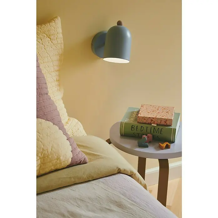 Nordlux Aplique de pared Gaston - 15 W, An x Pr x Al: 11,5 x 19,5 x 19,5 cm, Azul, E27 - Una lámpara de pared azul con pomo de madera cuelga sobre una mesita de noche con libros y juguetes en una acogedora habitación infantil.