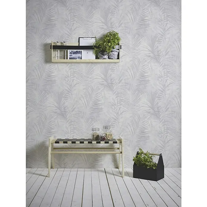 A.S. Création Neue Bude 2.0 ED II Vliestapete Palme - Grau, Floral, 10,05 x 0,53 m - Innenaufnahme eines Raumes mit einer Wandregal- und Sitzbankkombination aus hellem Holz, die mit verschiedenen Gegenständen dekoriert sind.
