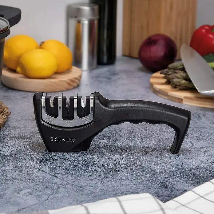 3 Claveles Afilador de cuchillos - Negro - Primer plano de un afilador de cuchillos 3 Claveles con mango sobre una encimera de cocina, rodeado de alimentos.