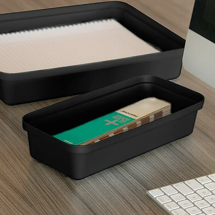 Sunware Sigma home Aufbewahrungsbox Pencil - L x B x H: 27 x 12,9 x 6 cm, Kunststoff, Schwarz - Das Bild zeigt zwei schwarze Schreibtischablagen, eine mit Papier und die andere mit einem Pantone-Farbführer, auf einem Schreibtisch.