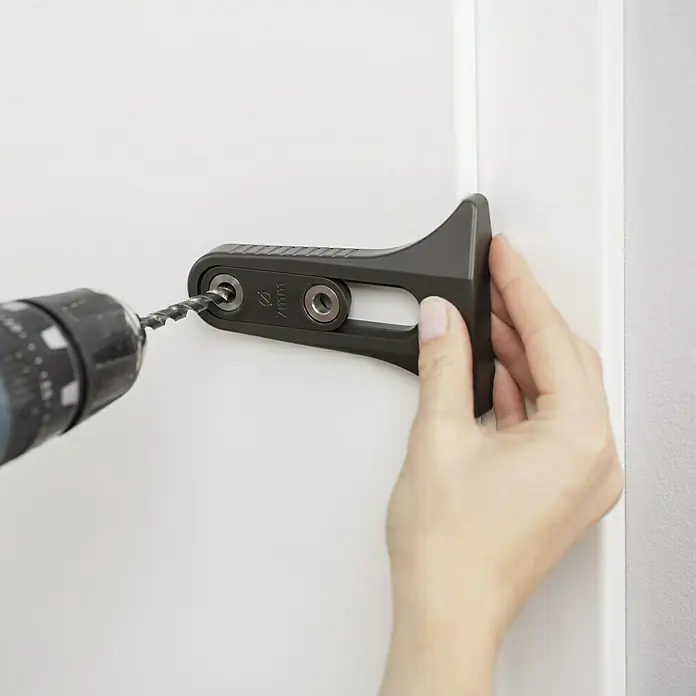 Bohrschablone - Gesamtstückzahl: 1 Stk., Durchmesser: 7 mm - Eine Person bohrt mit einem Bohrer durch eine graue Bohrschablone in eine weiße Tür. Die Bohrschablone ist ein Werkzeug zur Unterstützung beim Bohren.