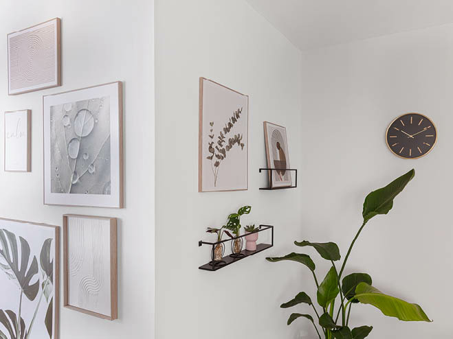 Gerahmte Bilder an der Wand, schwarzes Wandregal, Wanduhr und eine große Pflanze
