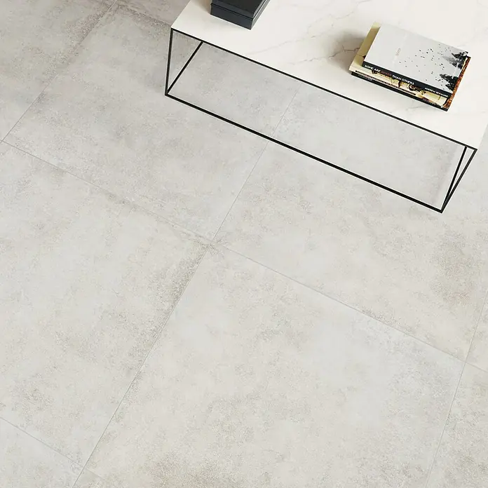 Feinsteinzeugfliese Savanna - 59,7 x 59,7 cm, Gris, Matt - Nahaufnahme von hellgrauen Bodenfliesen, ergänzt durch einen minimalistischen Tisch mit Büchern, der die moderne Ästhetik des Raumes unterstreicht.