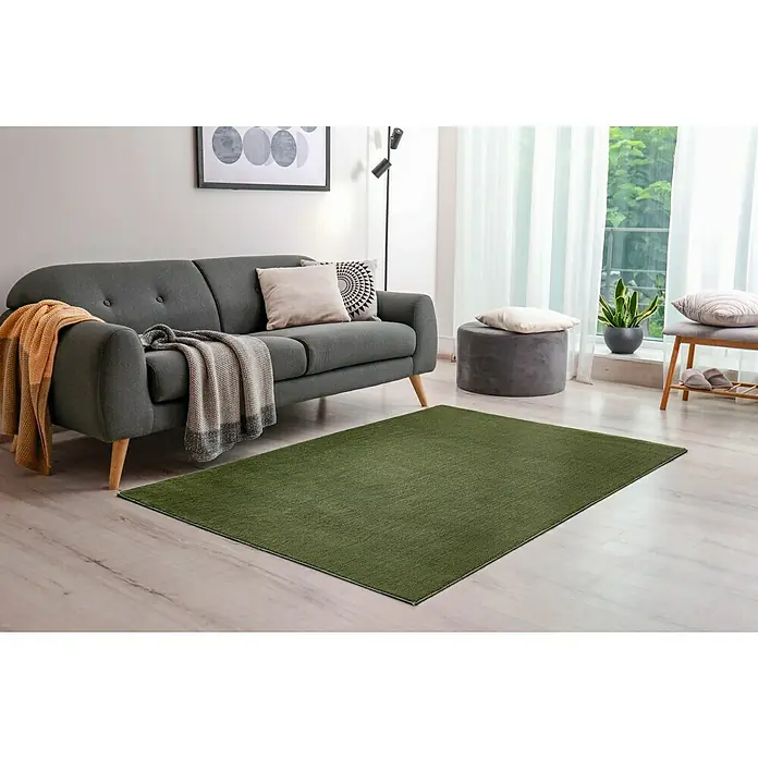 Hochflorteppich Lauria - Dunkelgrün, 230 x 160 cm, 100 % Polyester - Ein satter, grüner Teppich liegt im Wohnzimmer und verleiht dem Raum eine gemütliche Atmosphäre. Die Couch und das Tageslicht sorgen für Ambiente.