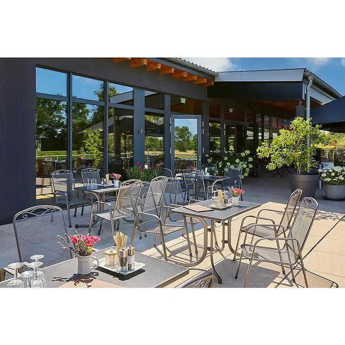 Gartenmöbel-Set Zingst/Boulevard I - 5 -tlg., Stahl, Mecalit, Eisengrau, Schiefer - Einladende Terrasse mit Tischen und Stühlen vor einem modernen Gebäude, ideal für entspannte Mahlzeiten im Freien.