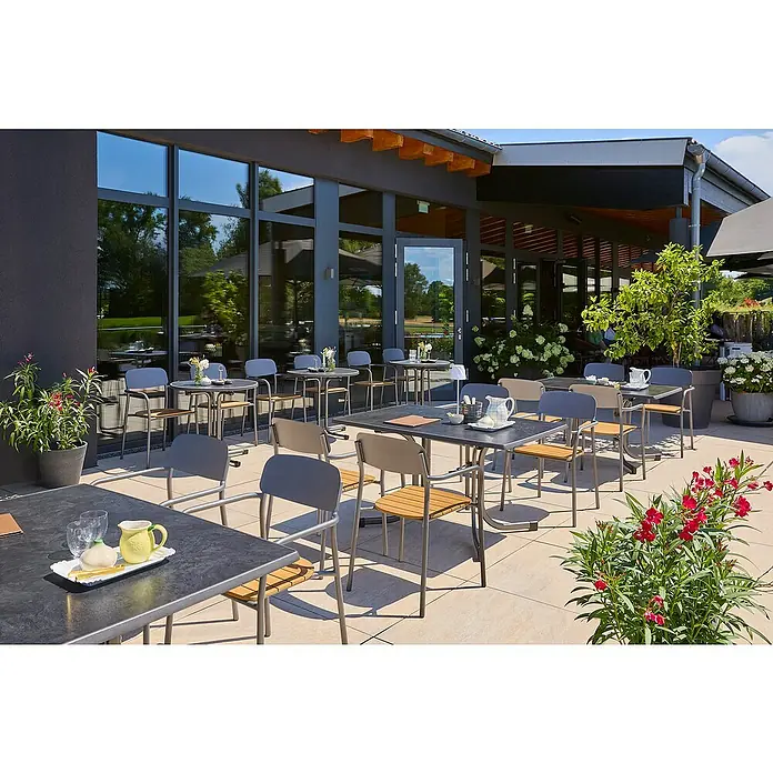 MFG Gartentisch Boulevard - L x B: 132 x 90 cm, Stahl, Mecalit, Schiefer, Klappbar - Außenansicht eines Restaurants mit Tischen und Stühlen. Die Tische sind mit Geschirr und Dekor gedeckt, im Hintergrund Fenster und Pflanzen.