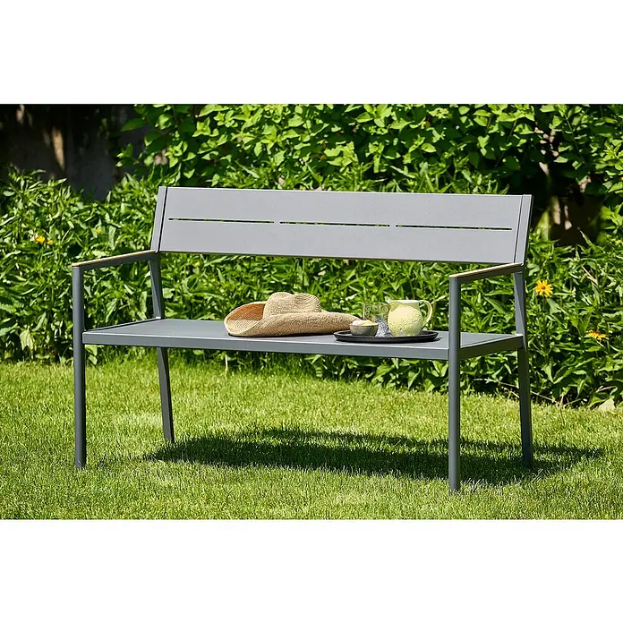 Sunfun Maja Gartenbank - B x T x H: 126 x 55 x 85 cm, Aluminium, Polywood, Night-Grey - Eine graue Gartenbank mit einer Pitcher und einem Hut auf dem Sitz vor grünem Hintergrund.