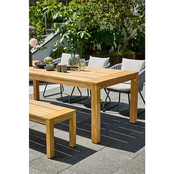 Sunfun Gartenmöbel-Set Laura/Maja - 5 -tlg., Akazie, Seilgeflecht, Naturbraun/Grau-Beige - Ein Holztisch mit passender Bank und Stühlen im Freien, ideal für Garten oder Terrasse, umgeben von üppigem Grün und Pflanzen.