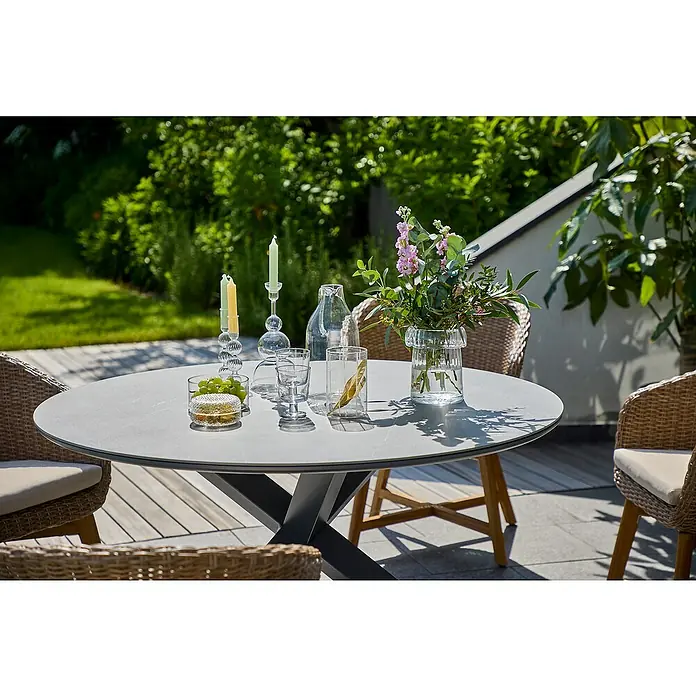 Sunfun Maja Gartentisch rund - Ø x H: 130 x 75 cm, Aluminium, Night-Grey - Ein runder Gartentisch mit verschiedenen Dekorationsgegenständen wie Kerzen, Gläsern und einer Blumenvase auf einer Terrasse.