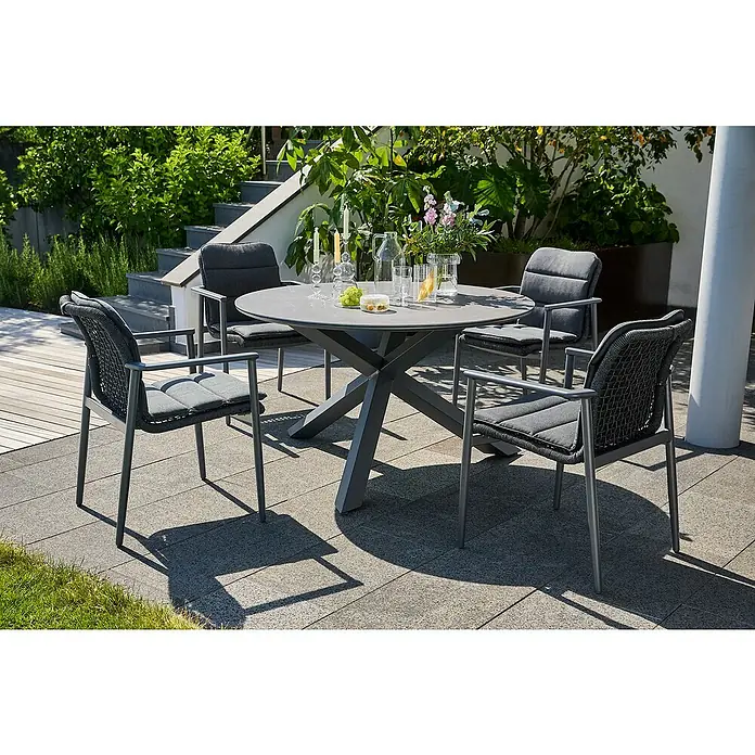 Sunfun Maja Gartentisch rund - Ø x H: 130 x 75 cm, Aluminium, Night-Grey - Ein stilvolles Outdoor-Essset mit einem runden Tisch und vier Stühlen mit grauen Polstern auf einer sonnigen Terrasse.