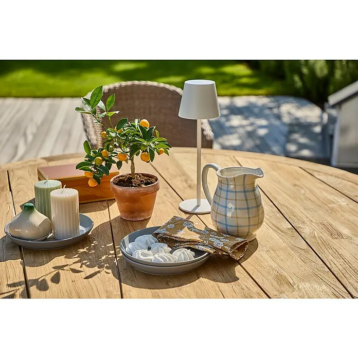 Sunfun Garten-Tischplatte - Durchmesser: 150 cm, Teak, Natur - Ein Gartentisch mit einem kleinen Orangenbaum, Kerzen, einer Lampe und einer blau karierten Krug für ein entspanntes Outdoor-Ambiente.