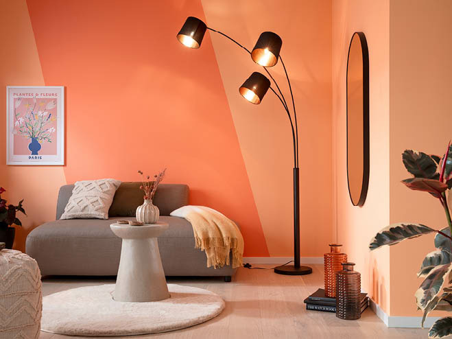 Kleine Couch mit Teppich und Tisch, daneben eine Stehlampe und die Wand in der Trendfarbe Peach Fuzz gestrichen
