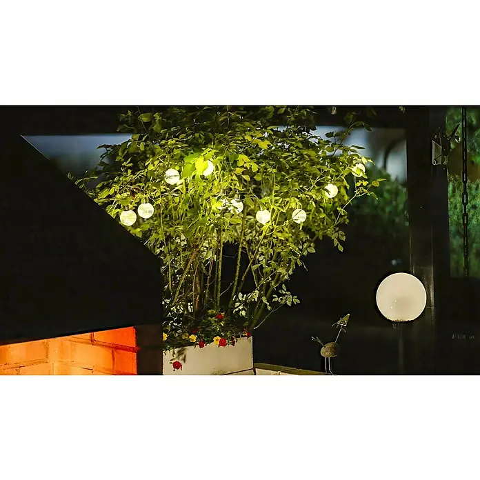 BAUHAUS LED-Solar-Lichterkette Shine - Außen, 4,8 m, Warmweiß - Stimmungsvolle Gartenbeleuchtung mit kugelförmigen LED-Lichtern an einem üppigen Strauch, der in einem Pflanzgefäß auf einer Terrasse steht.