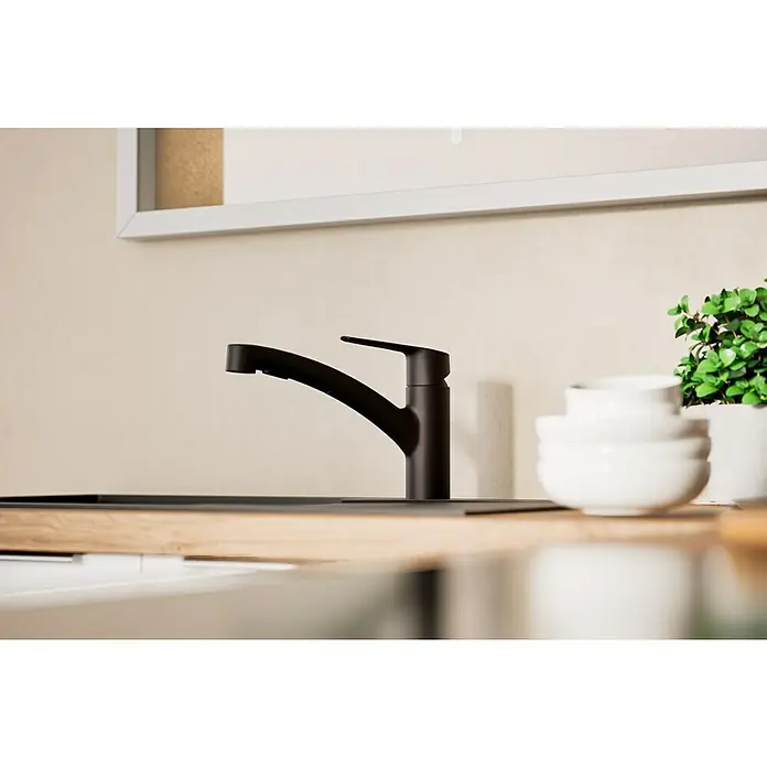Grohe QuickFix Start Spültischarmatur - Schwarz, Schwenkbar, Matt - Ein moderner, schwarzer Küchenhahn steht auf einer hellen Arbeitsplatte neben weißen Schüsseln und einer grünen Pflanze.