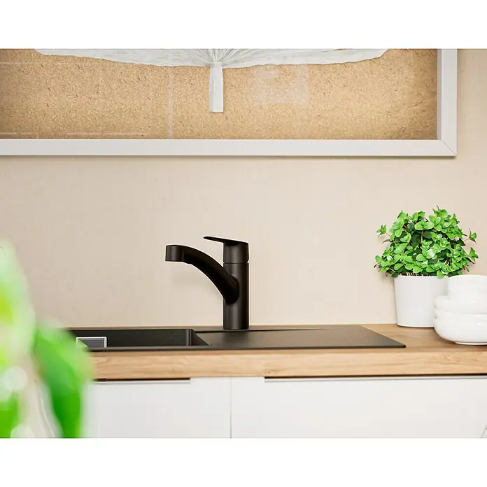 Grohe QuickFix Start Spültischarmatur - Schwarz, Schwenkbar, Matt - Eine moderne, mattschwarze Küchenarmatur mit Einhebelmischer auf einer Arbeitsplatte mit Spüle, ergänzt durch eine Zimmerpflanze und Geschirr.