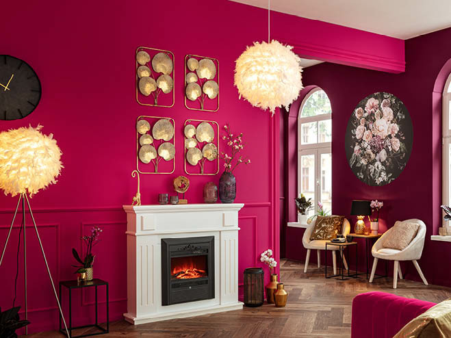 Stehleuchte und Pendelleuchte mit Federn, die Wände in Magenta gestrichen im Wohnraum und ein elektrischer Kamin in der Mitte