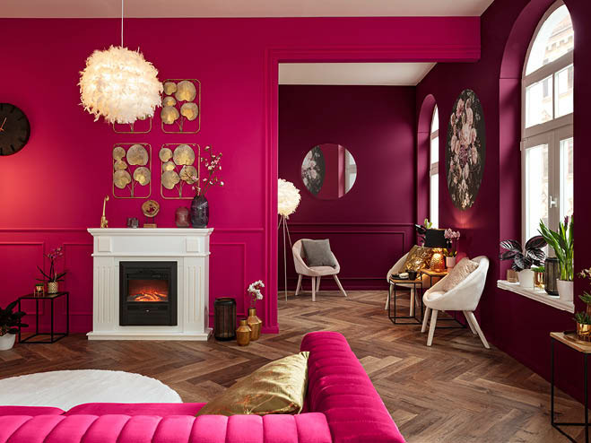 Wohnzimmer in knalligen Magenta gestrichen, mit elektrischem Kamin und Stühlen sowie einer pinken Couch