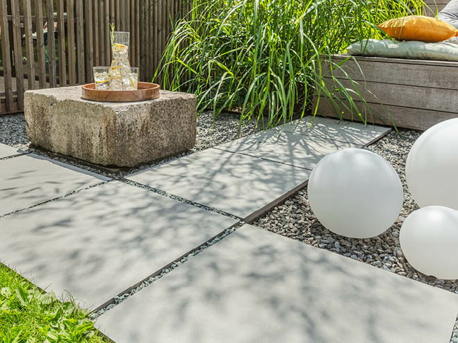 Graue Terrassenplatten im Garten als Weg, dazwischen Kies und mit Leuchtkugeln dekoriert