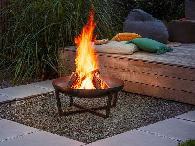 Feuerschale im Garten bei Nacht mit Feuer, dahinter eine Sitzecke