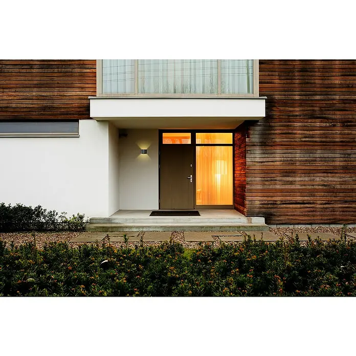 E2 elektro LED-Außenwandleuchte Ebla - 7 W, 10 x 13,5 x 12 cm, Anthrazit, IP65 - Moderne Hausfassade mit Holzelementen und einer einladenden Eingangstür. Das Licht strahlt warm nach aussen.