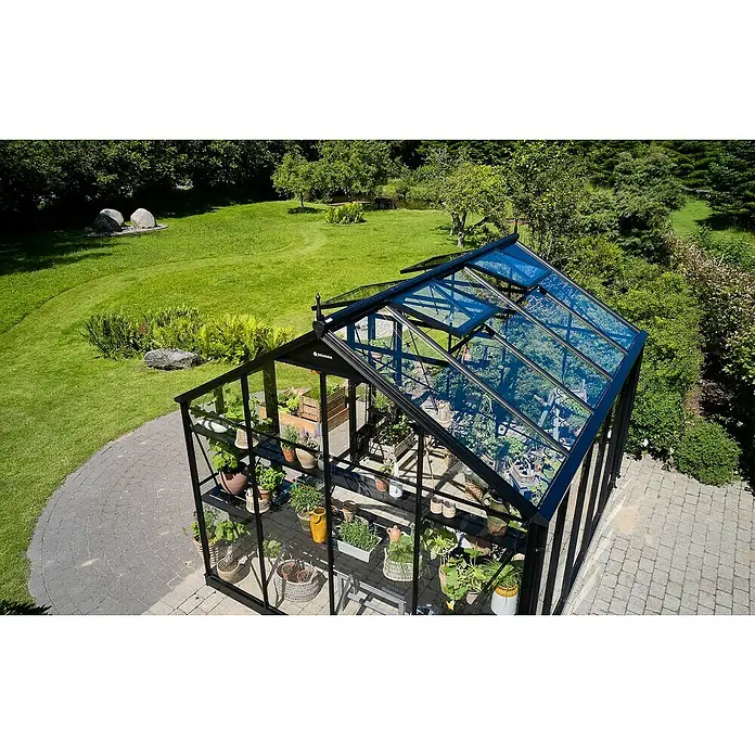Juliana Gewächshaus Jubii 60 - Außenmaß inkl. Dachüberstand (B x T): 368 x 296 cm, Material Seitenwand: Glas, 3 mm, Schwarz - Ein Gewächshaus mit Pflanzenregalen, umgeben von einem Garten mit Rasen, Bäumen und Steinen. Die offene Dachluke sorgt für Belüftung.